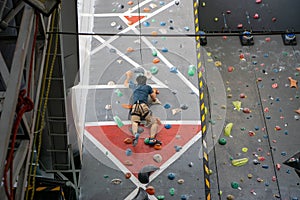 Person mit Sicherheitsgurt und Kletterschuhen klettert auf einer Wand mit Griffen in einer Indoor-Kletterhalle