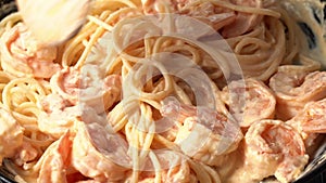 Person mixing pasta with shrimp and cream sauce in frying pan, spaghetti with seafood and rich cream