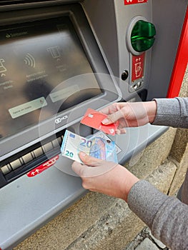 Person operating an ATM, with cash and card in hand in a street in Spain, in a street in Salamanca, Castilla y Leon, Spain,