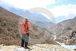 Person in orange windbreaker stands on mountainside in Himalayas photo