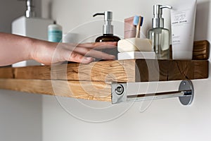 person organizing toiletries on a wooden shelf with metal brackets