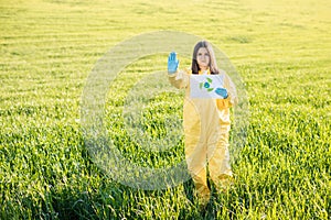 Person in overalls holds paper with a call to save the planet while standing on green field on sunset and the other hand shows a