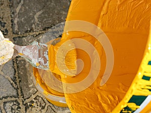 A person with a paint brush pouring yellow paint into a small bucket out of bigger bucket
