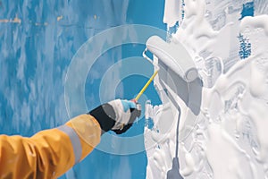 person with paint roller coating white paint over a blue wall