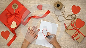 Person painting heart sign on paper, hand-made gift boxes on wooden background