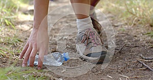 A person picks up a plastic bottle while walking on a dirt path and collecting trash
