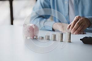 Person with pile of coins and piggy bank, money saving concept for future use.