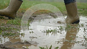 Person with pink boots and blue umbrella splashing in the puddle. girl in raincoat and rubber boots jumping into puddle