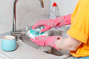 A person in pink rubber gloves is washing dishes. Close up of kitchen sink and hands. View from the shoulders. Housework