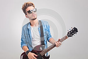 Person playing guitar in studio while wearing sunglasses