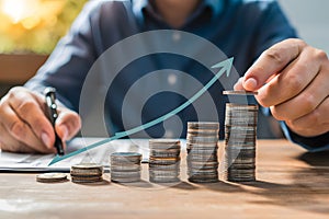 Person pointing to stacks of ascending coins, symbolizing growth and wealth against blurred background