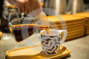 Person pouring coffee in a mug on a wooden tray