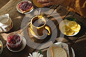 Person pouring tea from teapot during morning breakfast.