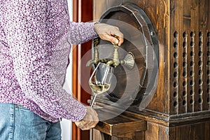 Person pouring wine from a wine barrel. Mature sommelier in winery basement pouring red wine into long-stemmed wine glass