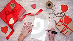 Person preparing to paint on paper, hand-made gift boxes on wooden background