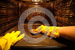 A person in protective gloves washes the dirty oven from traces of food inside with the light on