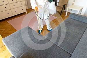 Person in protective suit with decontamination sprayer bottle disinfecting household and furniture photo