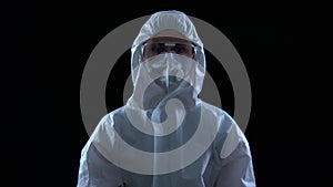 Person in protective suit shaking head on black background, virus leak, caution