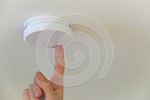 A person push the test button on a automatic smoke detector fire alarm in the ceiling.