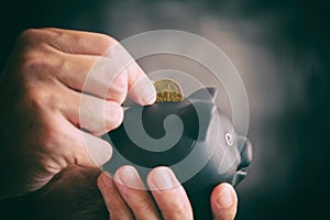 Person putting 20 euro cent coin into black piggy bank against black background