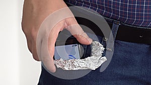 Person putting a smartphone in his pocket covered with foil