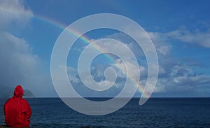 A person with a raincoat looking at the rainbow