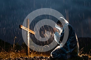 person in raincoat praying by cross during a downpour