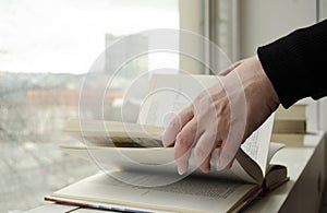 A person reading books near the window. Hands turns over book page