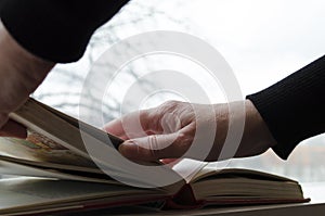 A person reading books near the window. Hands turns over book page