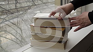 A person reading books near the window. Hands turns over book page