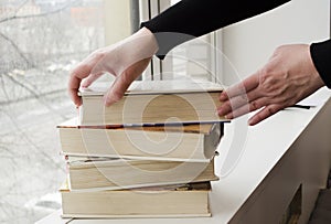 A person reading books near the window. Hands turns over book page