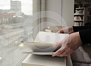 A person reading books near the window. Hands turns over book page