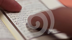 A person is reading from a small Quran and tracing the versions with the finger