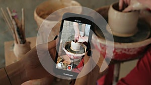 Person recording video on smartphone of how ceramist works on pottery wheel