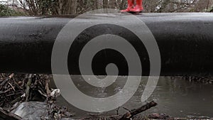 Person in red wellies carefully negotiating pipe over stream