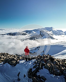 Person in a red winter coat on a pile of snow-covered rocks in a picturesque winter landscape