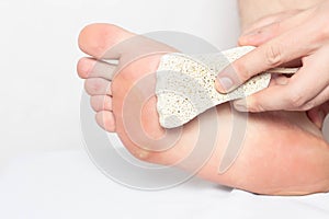 A person removes scrubs dry calluses and natograms from the sole of a foot with pumice stone, close-up, treatment, copy space,