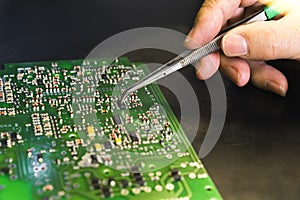 Person repairing printed circuit board PCB mounting electrical components by hand using tweezers. Precise repair-work