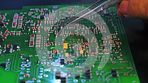 Person repairing printed circuit board PCB mounting electrical components by hand using tweezers. Precise repair-work