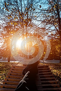 person resting in wooden hammock or bench in autumn park at sunset