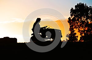 Person on a Ride On Lawn Mower on Farm at Sundown photo