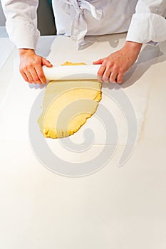 A pastry chef is rolling out dough on a table with a rolling pin. yellow dough and the worker is wearing a chef& x27;s uniform