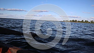 Person is rowing with a wooden oar on boat on a lake during sunny day