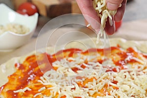 Person's hand adding grated cheese to pizza,  process of making pizza