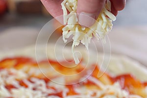 Person's hand adding grated cheese to pizza,  process of making pizza