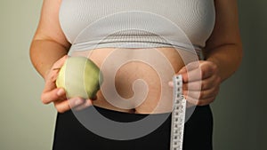 Person's hand holding green apple with grey measurement tape isolated on white background. Weight loss and dieting