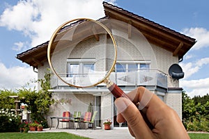 Person`s Hand Holding Magnifying Glass Over Luxury House