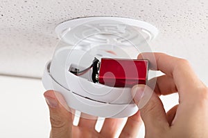 Person`s Hand Inserting Battery In Smoke Detector photo