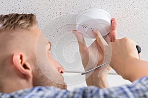 Person`s Hand Installing Smoke Detector On Ceiling photo