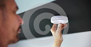 Person's Hand Installing Smoke Detector On Ceiling Wall